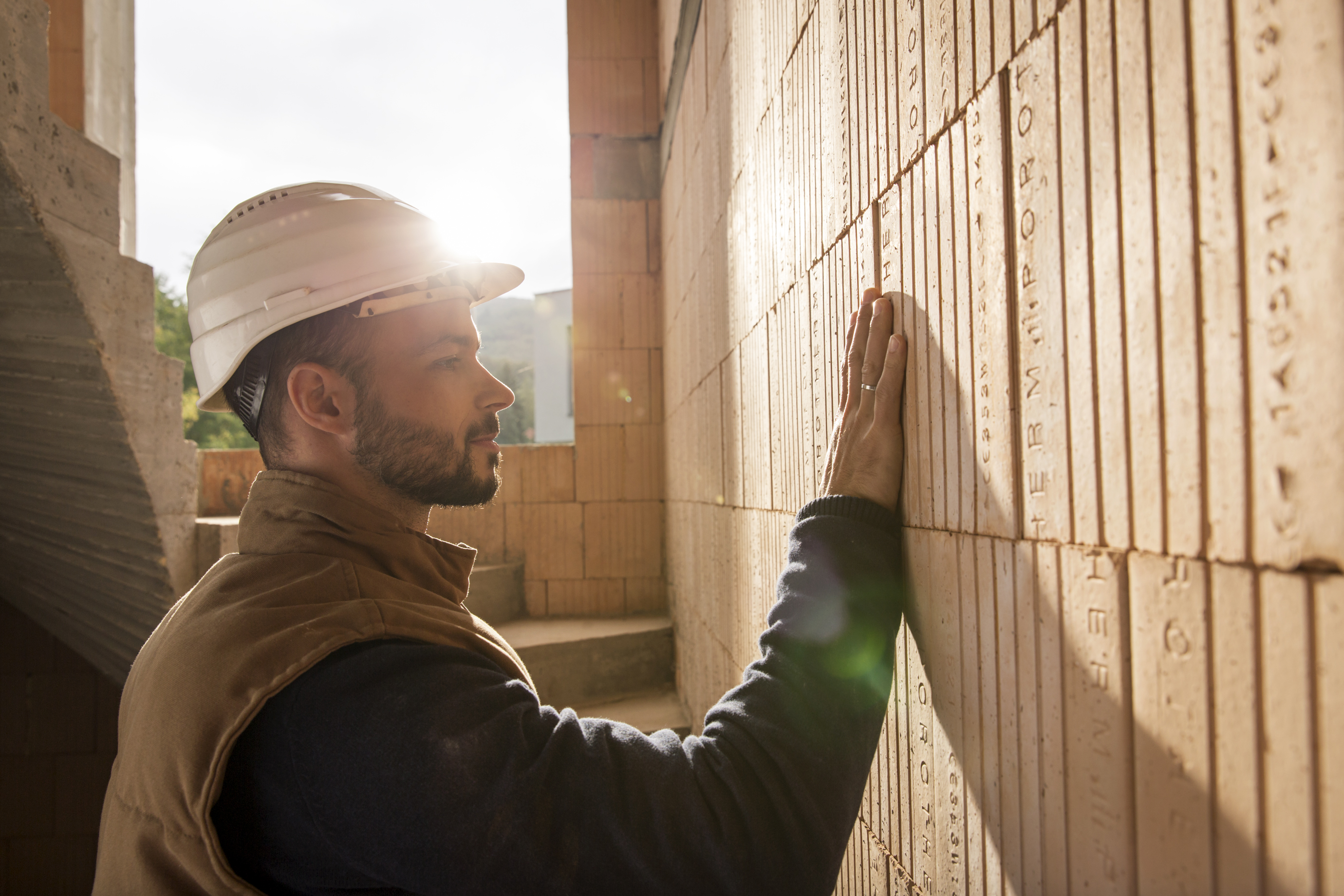 Man with safety helmet touching bare brick wall